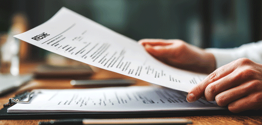 Close up; desk with paperwork; hands coming into left frame holding resume as if reviewing it